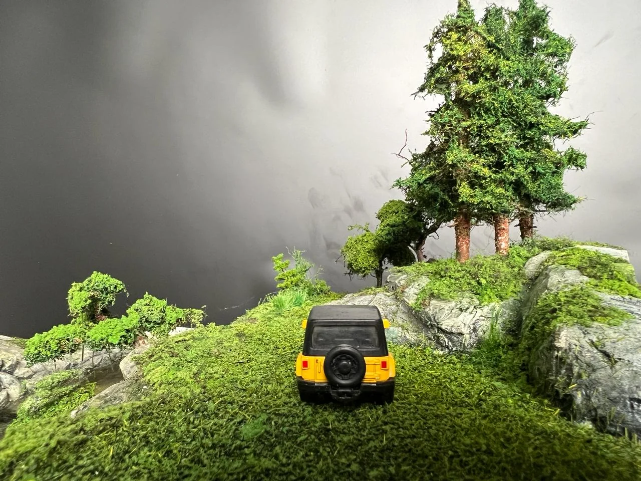 Miniature yellow vehicle entering a forested rocky landscape.