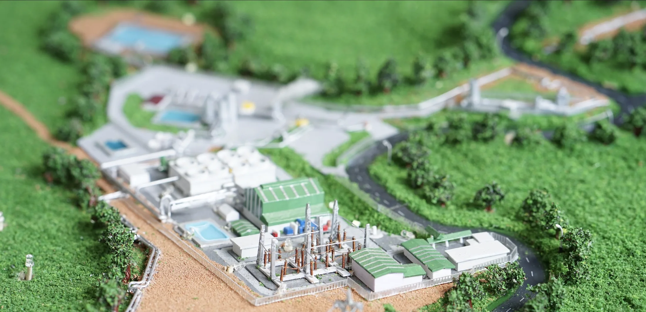 Close-up of Muara Laboh power plant model with facility, roads, and green terrain.